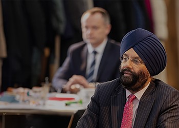 Attendee with a turban focusing intently at a conference, with another participant visible in the background.